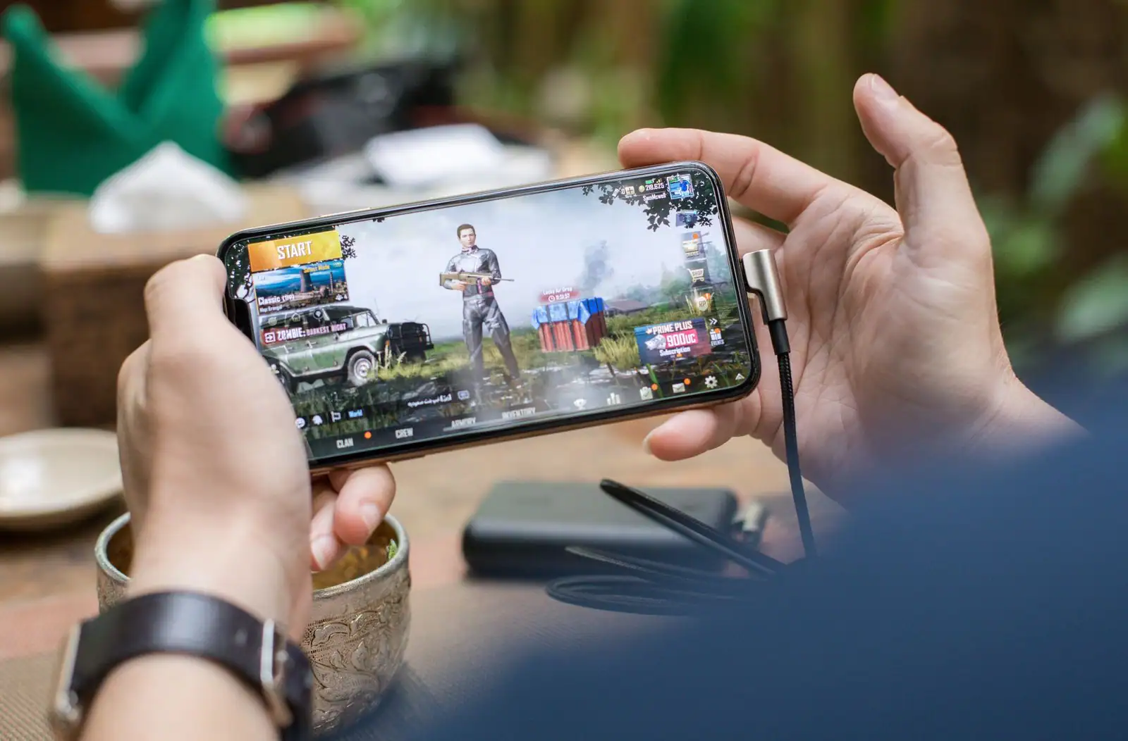 Mains tenant un smartphone en mode paysage pour jouer à un jeu mobile, en extérieur