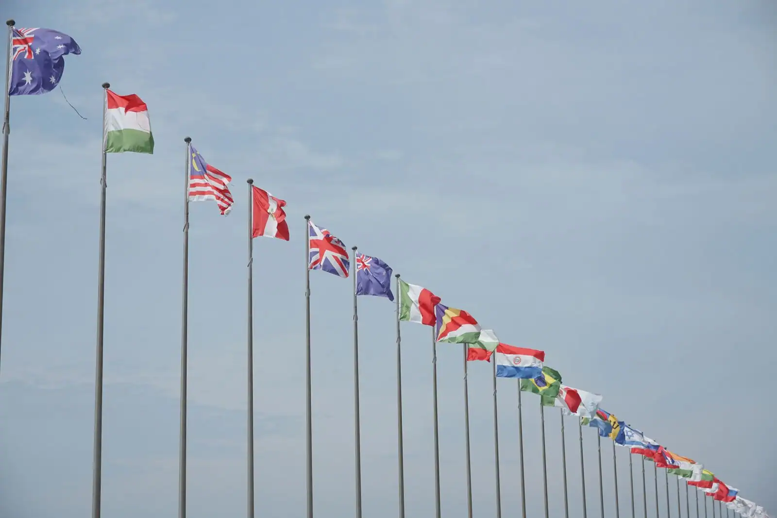 Drapeaux nationaux de plusieurs pays alignés sur des mâts devant un ciel dégagé