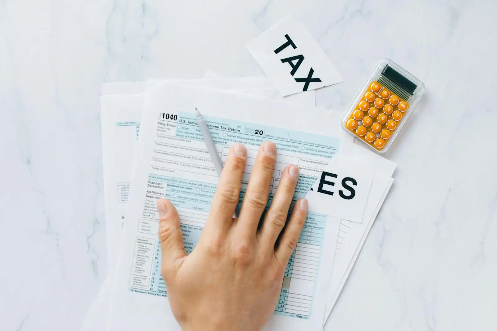 Personne calculant sa déclaration de revenus avec une calculatrice et des documents fiscaux posés sur un bureau