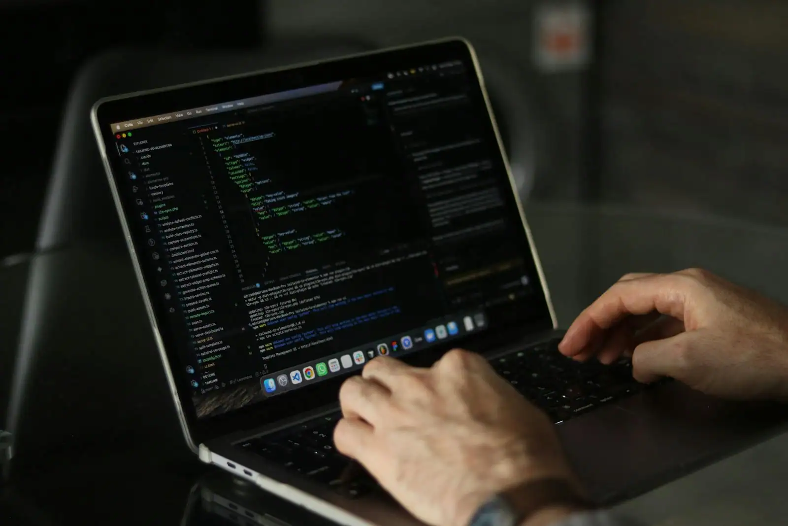 Les mains d'une personne tapent sur un ordinateur portable affichant un éditeur de code informatique