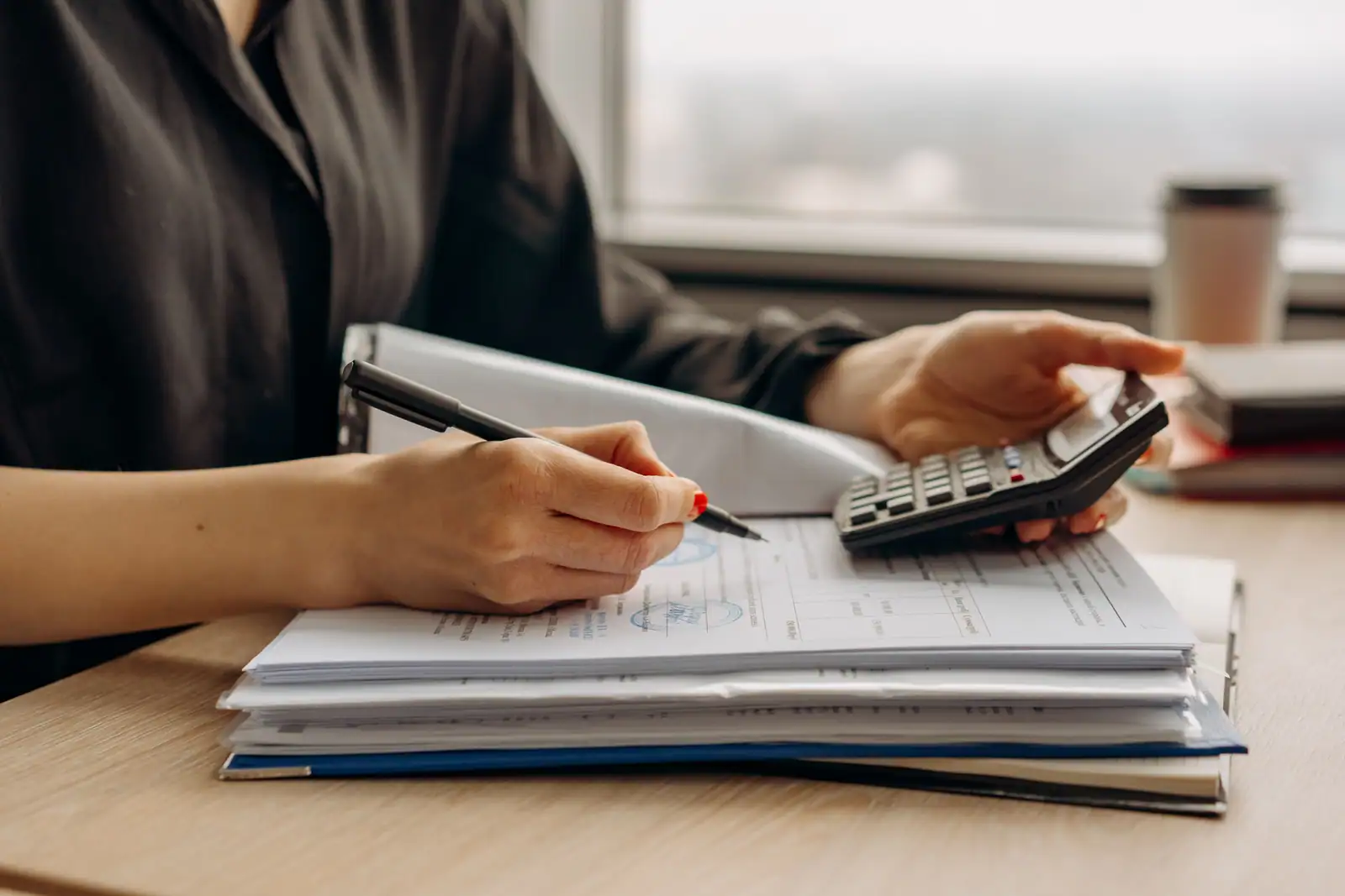 Une personne vérifie des documents bancaires à l'aide d'une calculatrice, installée à son bureau.