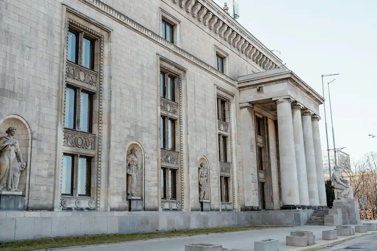 Façade en pierre d'un grand bâtiment institutionnel à colonnes, orné de statues, vu depuis la rue