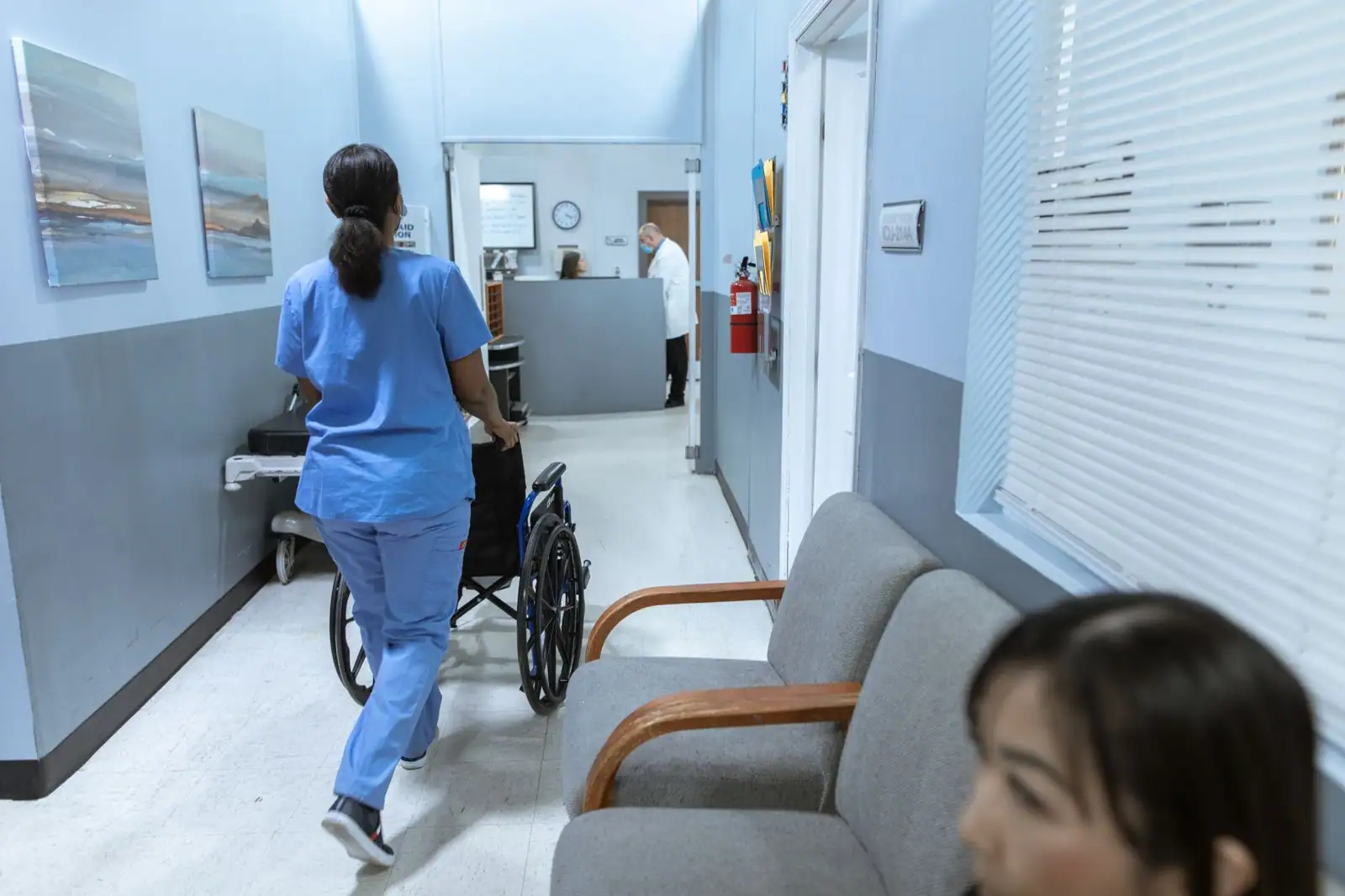 Infirmière en blouse poussant un fauteuil roulant dans le couloir d'un établissement de soins