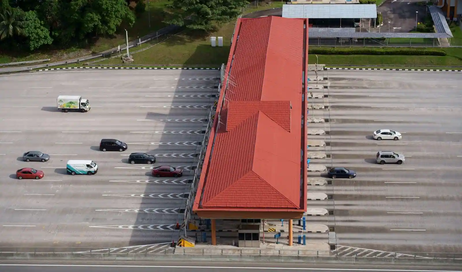 Vue aérienne d'une gare de péage autoroutière, ses cabines coiffées d'un toit rouge et des voitures circulant sur les voies.