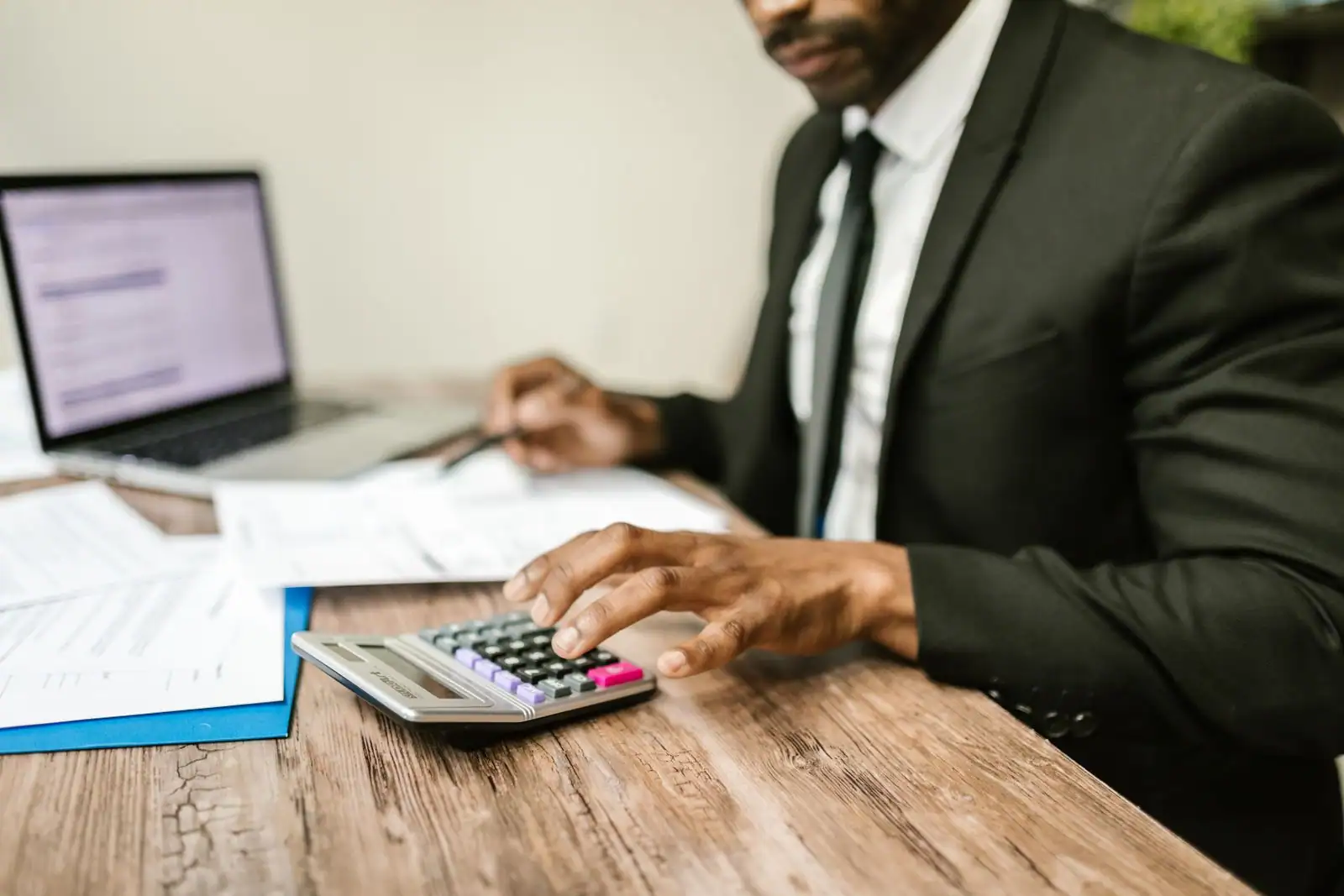 Personne utilisant une calculatrice à côté d'un ordinateur portable et de documents sur un bureau