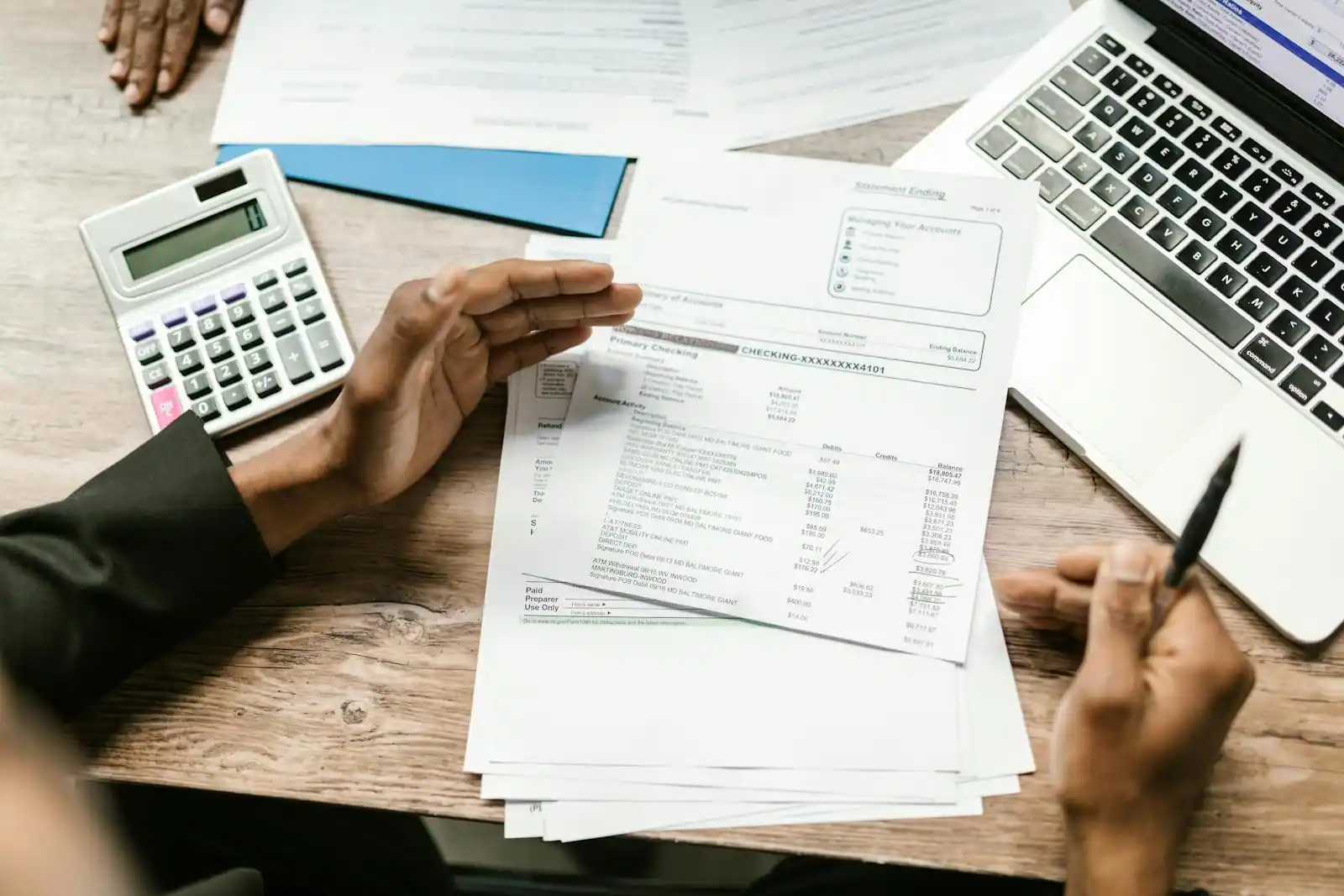 Deux personnes examinent des relevés financiers sur un bureau, avec calculatrice, ordinateur portable et stylo