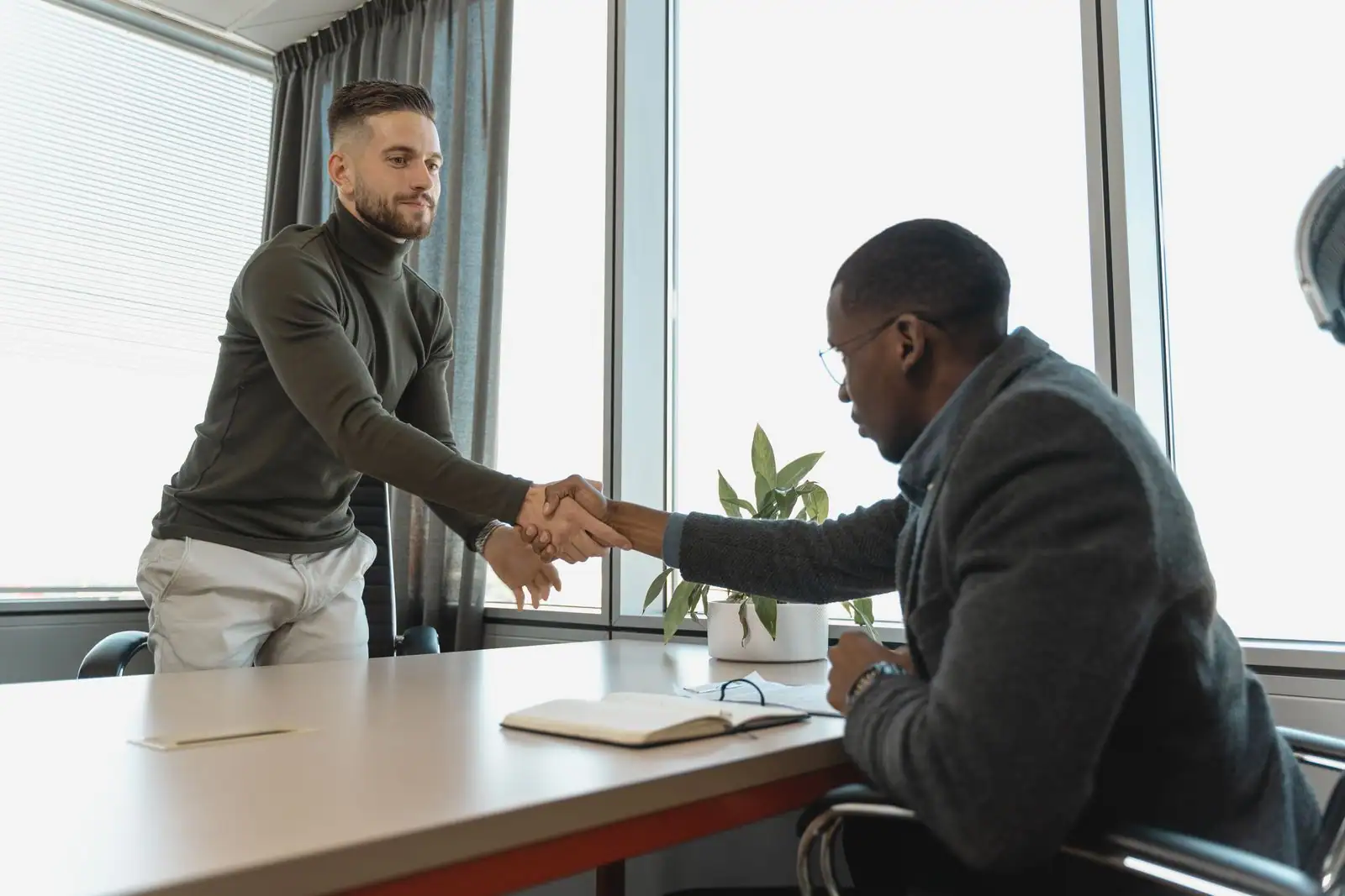 Entretien d'embauche dans un bureau : deux hommes se serrent la main au-dessus d'une table.