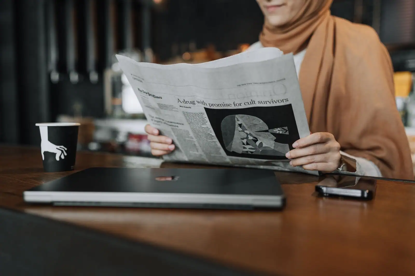 Une personne installée à une table lit un journal papier, illustrant le suivi de l'actualité locale