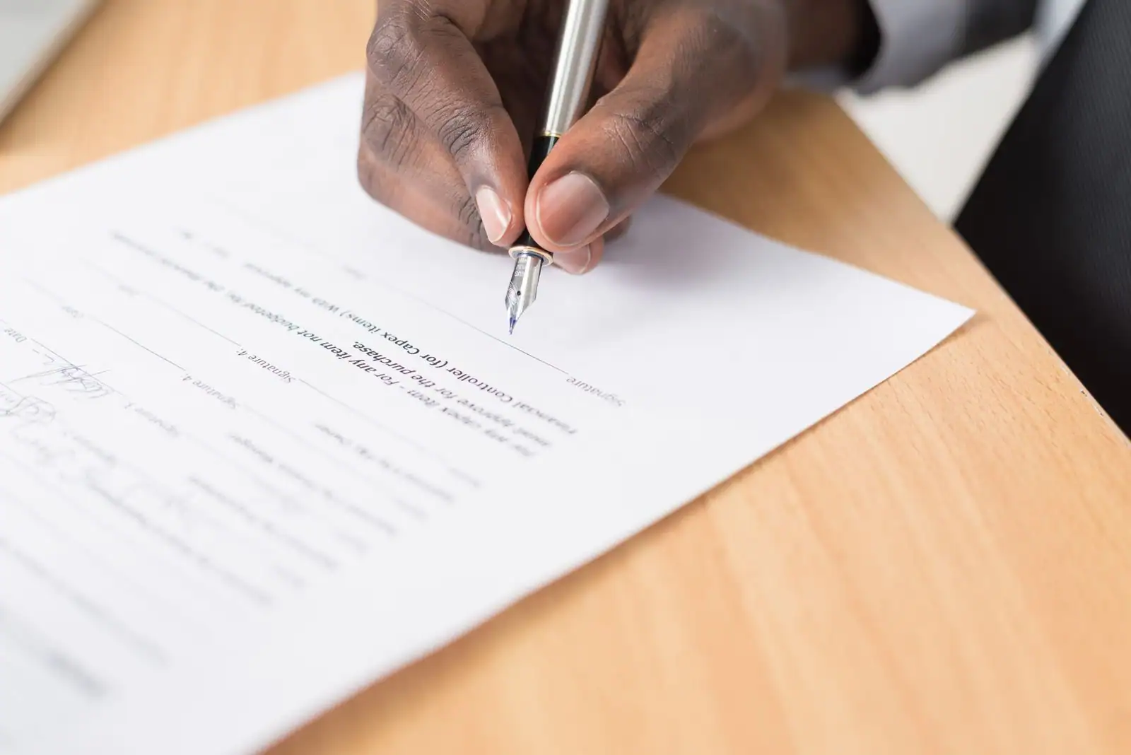 Main signant un document au stylo-plume sur un bureau en bois.