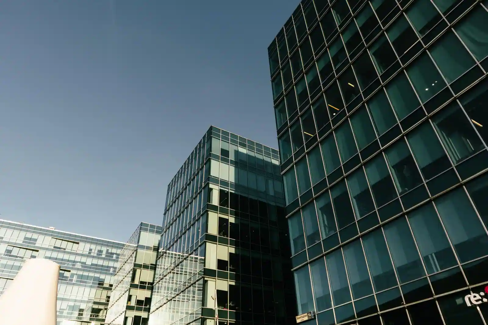 Tours de bureaux vitrées d'un quartier d'affaires moderne sous un ciel dégagé, en journée.