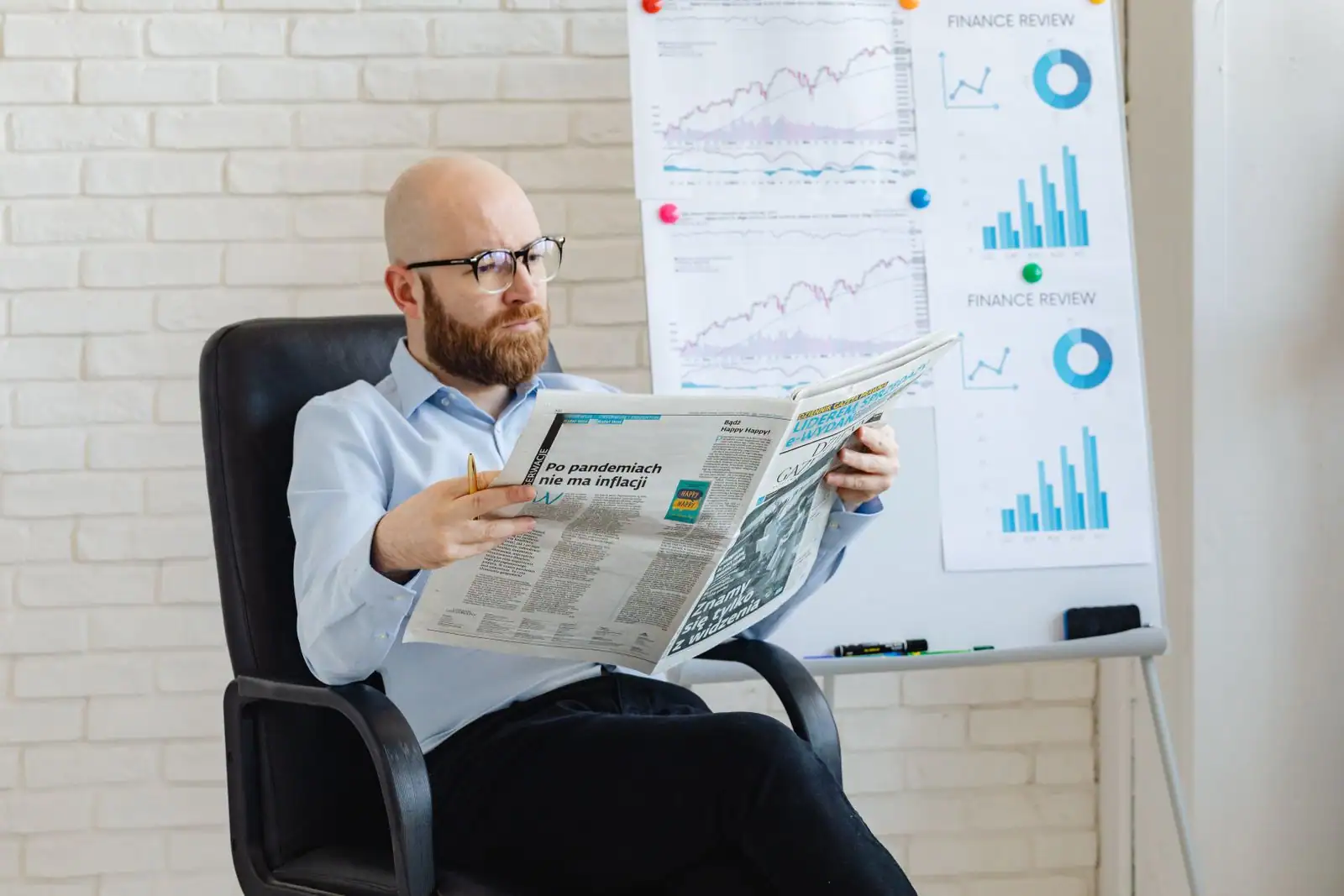 Homme lisant un journal économique devant un tableau couvert de graphiques financiers.