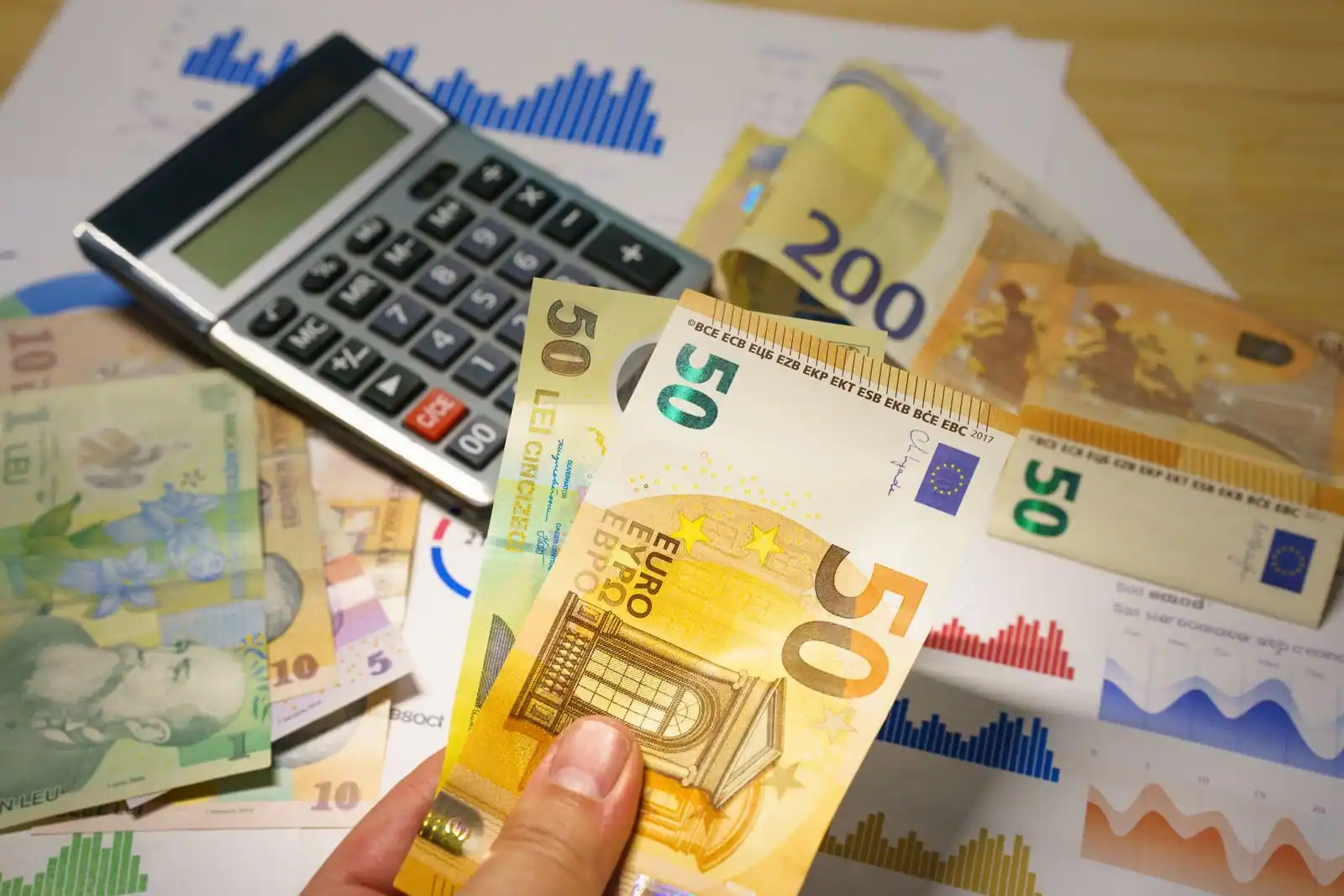 Main tenant des billets en euros près d'une calculatrice et de billets en devises étrangères.