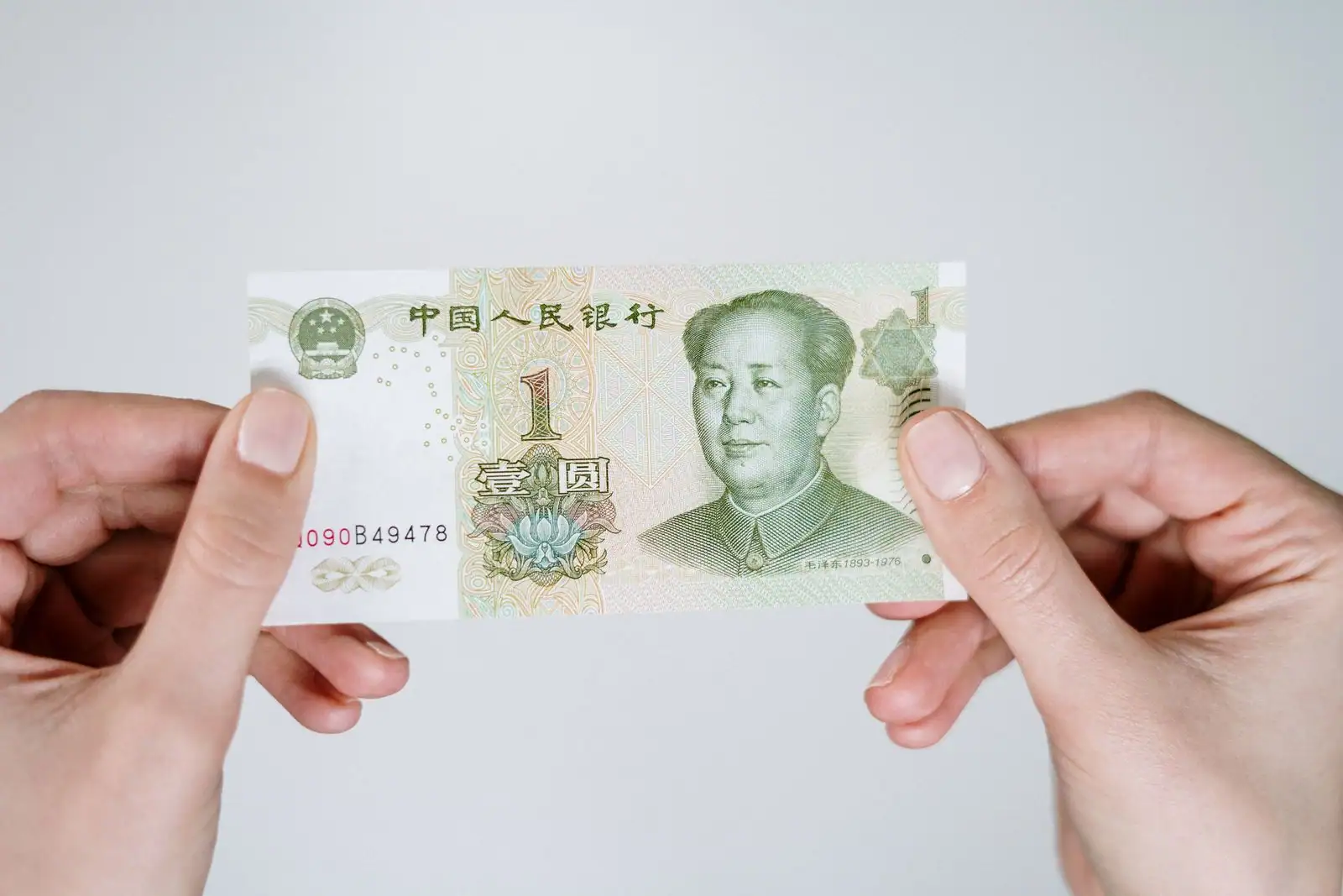 Gros plan sur un billet d'un yuan chinois tenu entre deux mains.