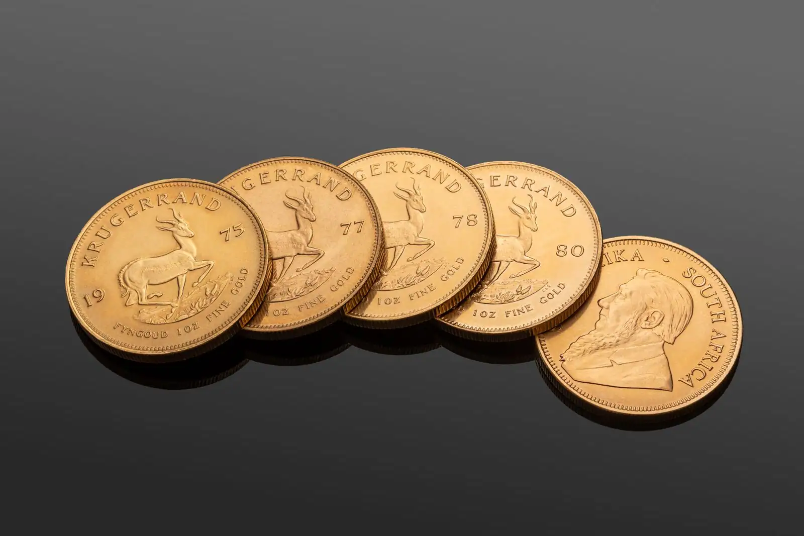 Pièces d'or Krugerrand d'une once posées sur une surface sombre réfléchissante.