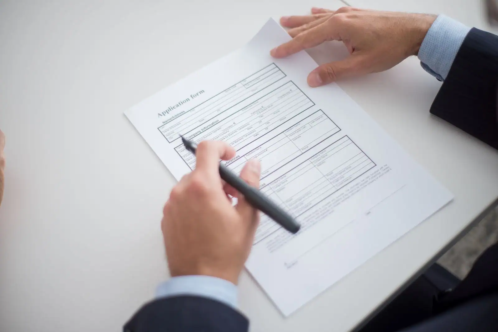 Mains remplissant un formulaire de candidature au stylo sur un bureau.