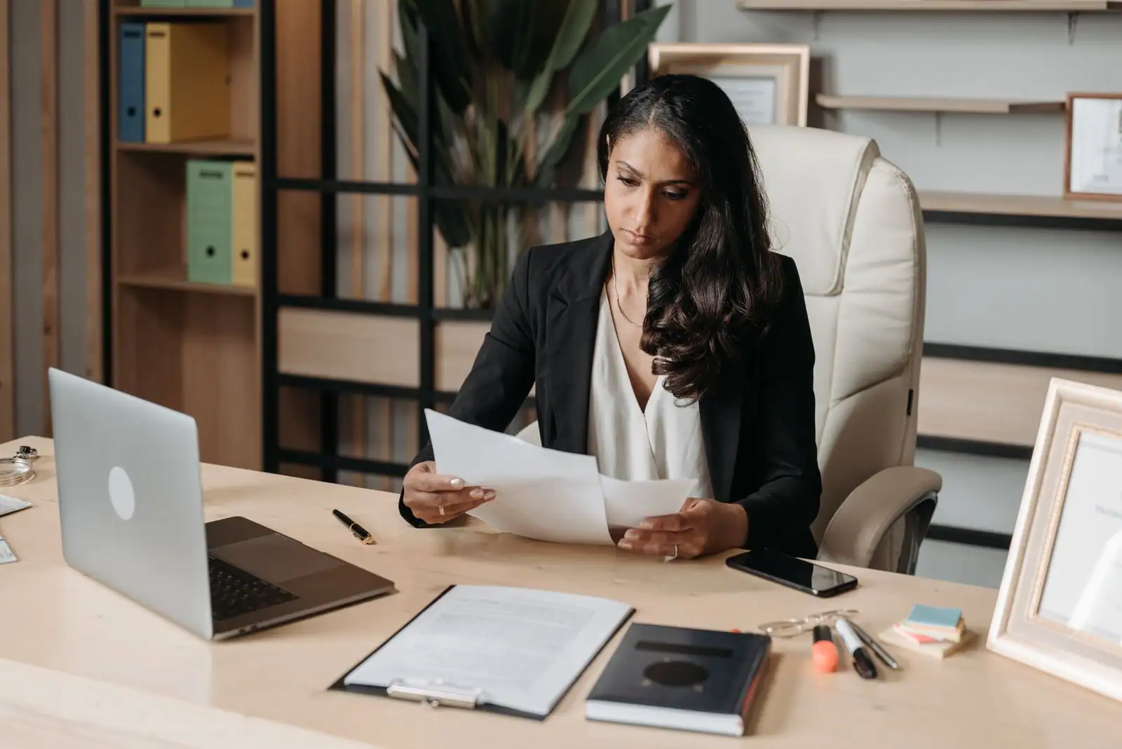 Entrepreneure examinant un document administratif à son bureau, ordinateur portable ouvert.