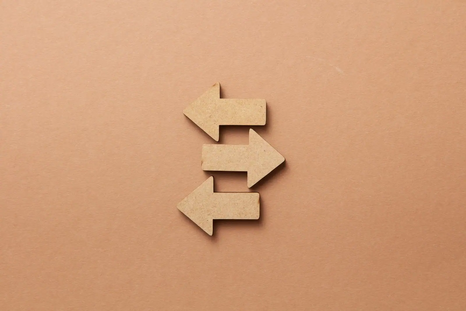 Trois flèches en bois pointant dans des directions opposées, sur un fond beige.