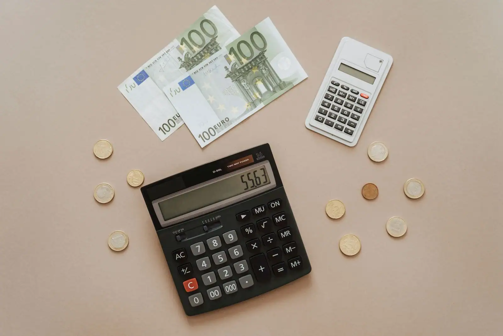 Calculatrices, billets et pièces en euros posés sur un fond neutre, évoquant le calcul de l'impôt.