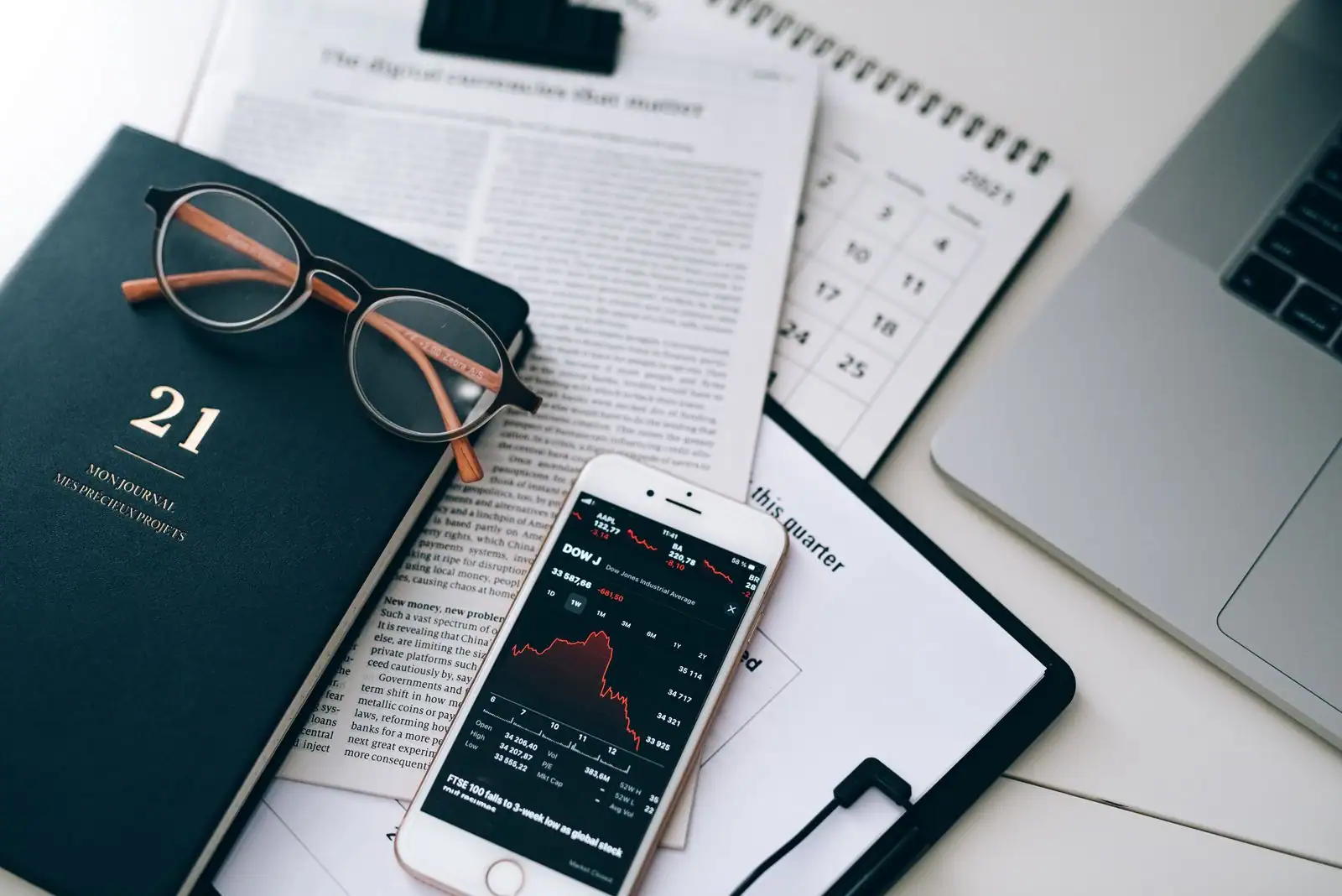Un smartphone affiche des cours de Bourse, posé sur les pages économiques d'un journal, près de lunettes.