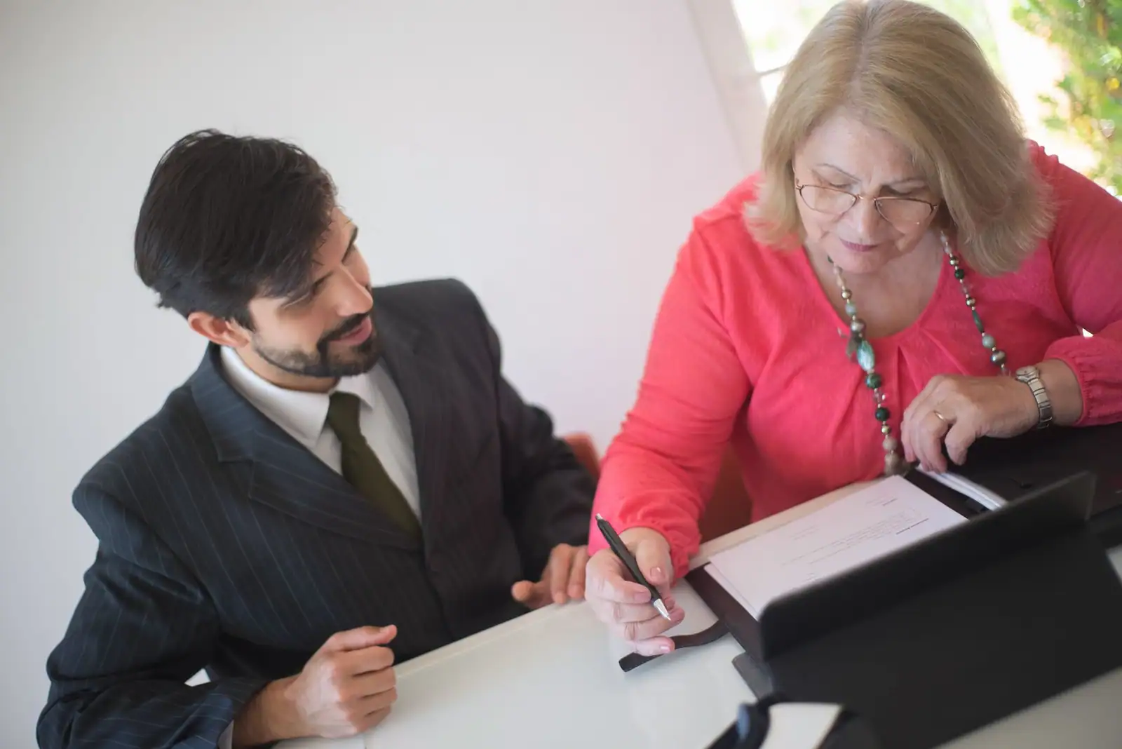 Femme âgée qui signe des documents avec l'aide d'un conseiller assis à ses côtés.