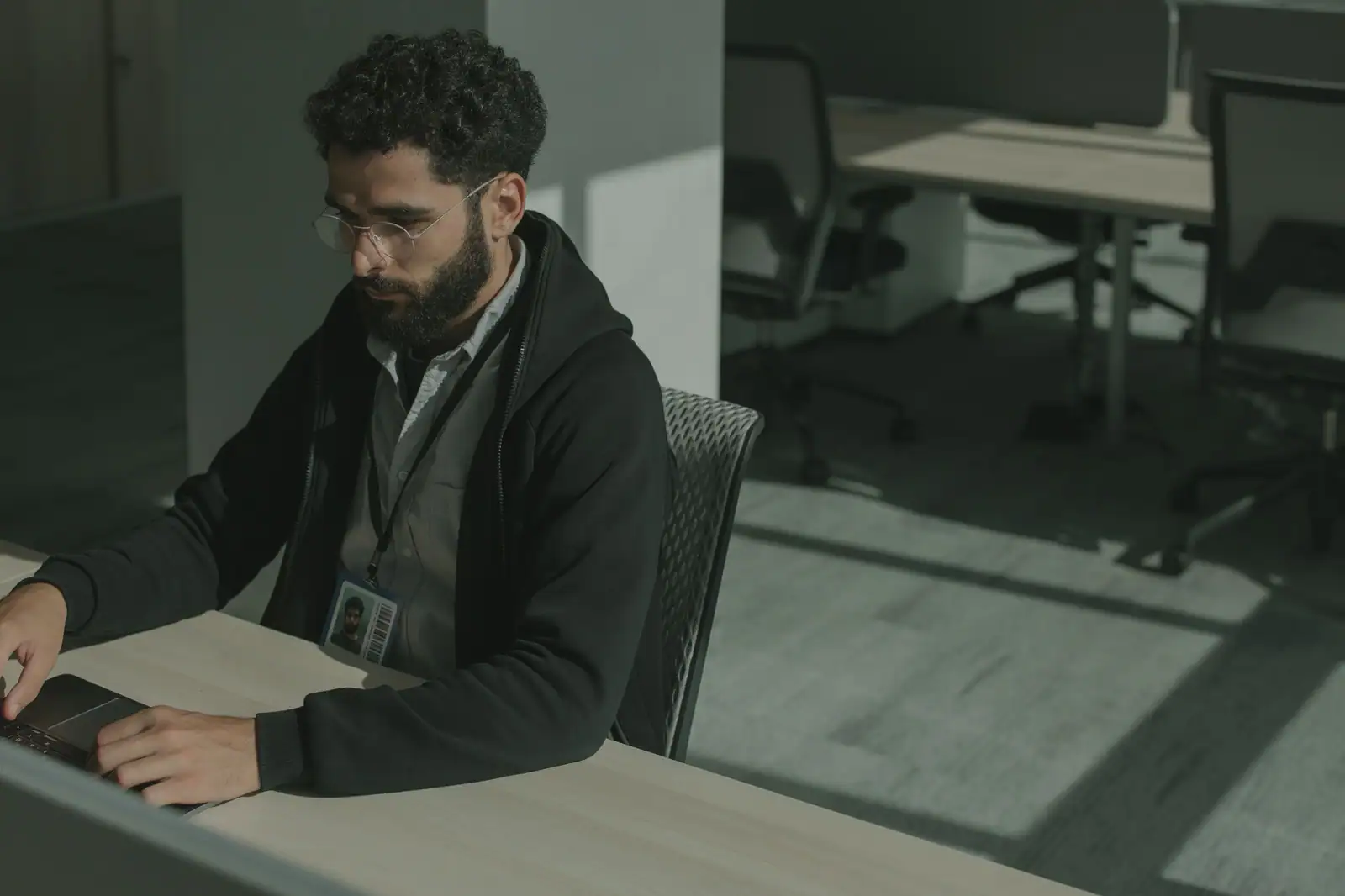 Un employé muni d'un badge professionnel travaille sur son ordinateur portable dans un bureau moderne.