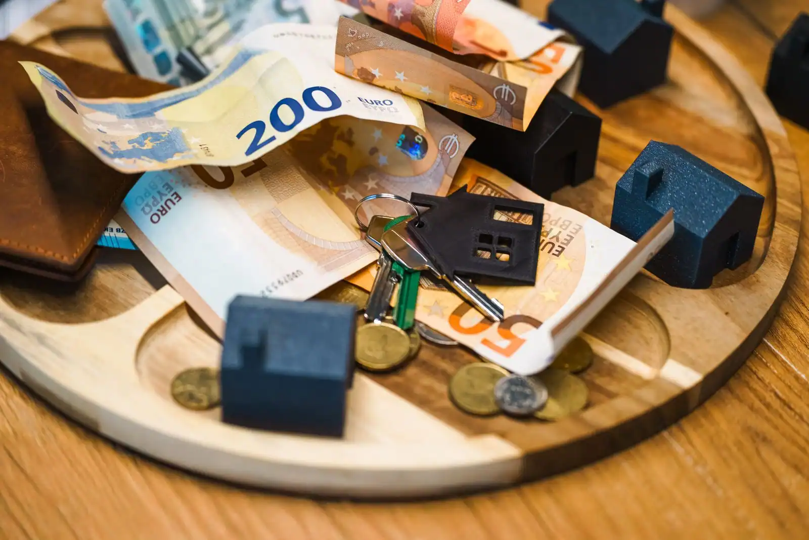 Maison miniature en bois posée près de piles de pièces, symbole de l'épargne pour un projet immobilier.